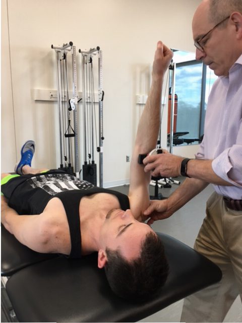 A man is being assisted by a physical therapist using a microFET®2 muscle tester.