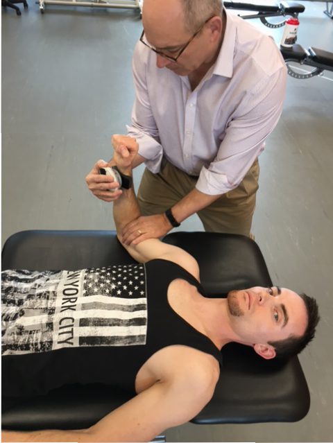 A man is being assessed by a physical therapist using a microFET®2 for his arm.