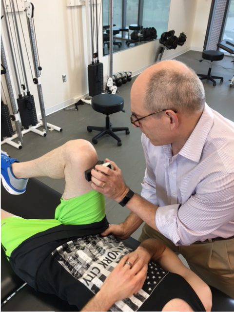 A man is getting his knee examined by a physical therapist using a microFET®2 muscle tester.
